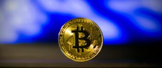 Close-up of a golden Bitcoin coin with a blurred blue abstract background, symbolizes digital currency.