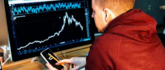 man holding black smartphone with flat screen monitor in front
